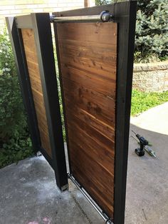 an open wooden door on the side of a building next to a sidewalk and trees