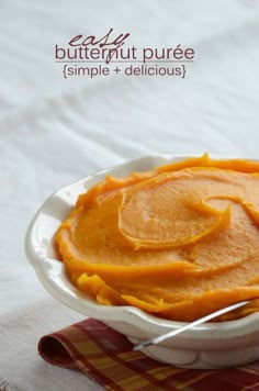 a white bowl filled with carrot puree on top of a red and yellow checkered table cloth