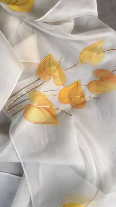 some yellow flowers are sitting on white fabric with gold stems and leaves sticking out of them