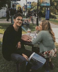 a man and woman sitting at a table in the park eating lunch together, smiling