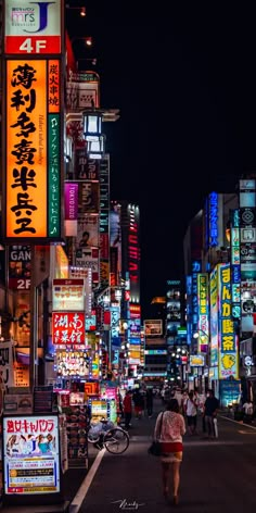 a woman walking down a street at night with neon signs on the buildings in the background