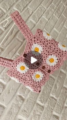 a crocheted pink purse with white and yellow daisies on it sitting on top of a bed