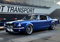 a blue mustang is parked in front of a transport truck with the words hot transport on it