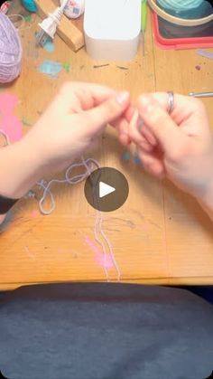 someone is making something with their hands on a wooden table in front of other crafting supplies