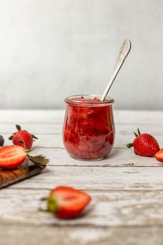 a jar filled with fruit sitting on top of a wooden table next to sliced strawberries