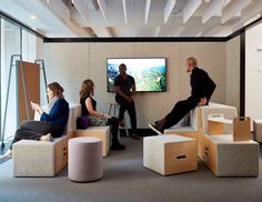 people sitting around in an office setting with large screens on the wall and windows above them