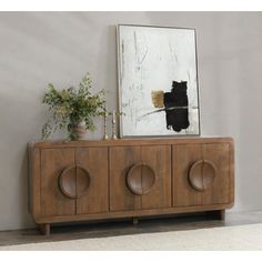 an art piece on top of a wooden cabinet next to a painting and potted plant