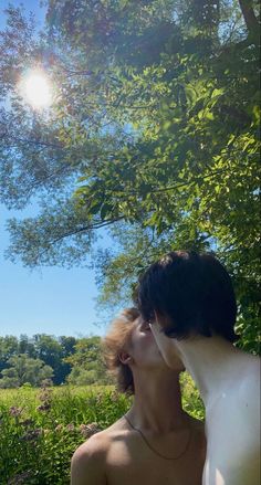 a man and woman standing under a tree with the sun shining in the sky behind them