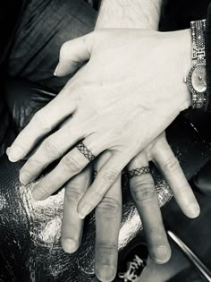 black and white photograph of two people's hands with tattoos on their fingers, sitting next to each other