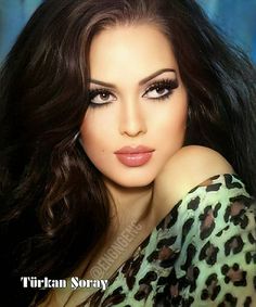 a woman with long dark hair and leopard print shirt posing for a photo in front of a blue background