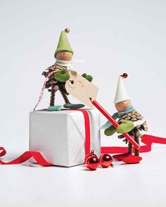 two small figurines sitting on top of a white present box with red ribbon