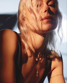 a woman with blonde hair wearing a black top and silver necklace, posing for the camera