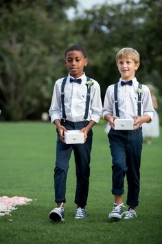 two young boys wearing suspenders and bow ties are standing in the grass holding small boxes