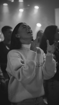 a woman standing in front of a crowd holding her hands up to the side and smiling