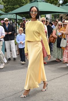 a woman in a yellow dress is walking down the street with people behind her and onlookers