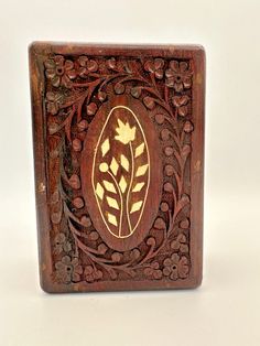 an intricately carved wooden box with flowers and leaves on the front, sitting on a white surface