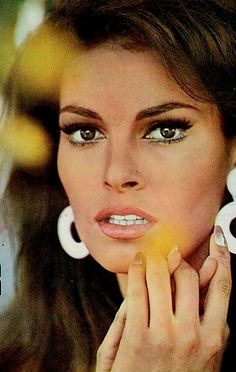 a woman with large white hoop earrings on her face looking at the camera and holding her hand to her mouth