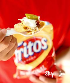 a person holding a spoon with some food on it in their left hand and a bag of chips in the other