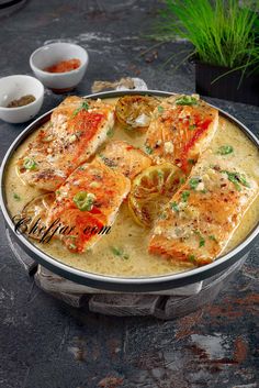 a pan filled with fish and vegetables on top of a stone table next to bowls