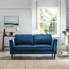 a blue couch sitting in front of a window next to a table with a vase on it