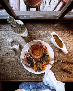 a white plate topped with meat and vegetables next to a cup of coffee on top of a wooden table