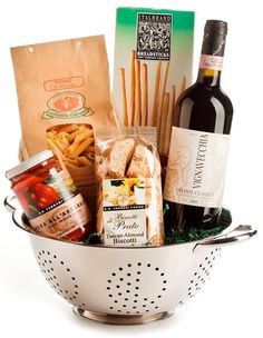 a white colander filled with wine, bread and other food items on a white background