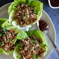 three lettuce wraps filled with meat and vegetables on a plate next to dipping sauce