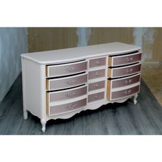 a white and pink dresser with drawers on it's sides, in front of a wall