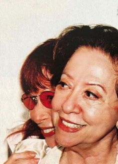 two women are smiling for the camera while wearing red sunglasses and white shirts, one is holding her arm around the other's shoulder