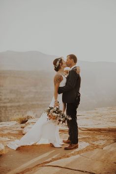 a bride and groom kissing on top of a mountain