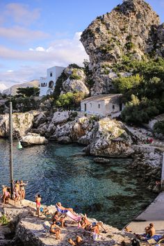 many people are swimming in the water near some rocks and cliffs, while others sunbathe