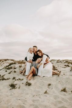 a family sitting together on the beach in front of some sand and grass, with their arms around each other