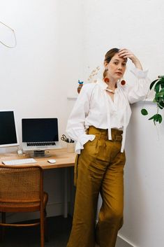 a woman standing in front of a desk with a computer on it and a potted plant behind her