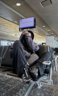 a man sitting on top of an airport chair holding a cell phone to his face