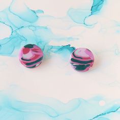 pair of pink and black marbled earrings laying on white background with blue swirls