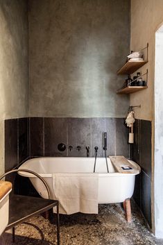 a bath tub sitting next to a wall with shelves on it's sides and a chair in front of it