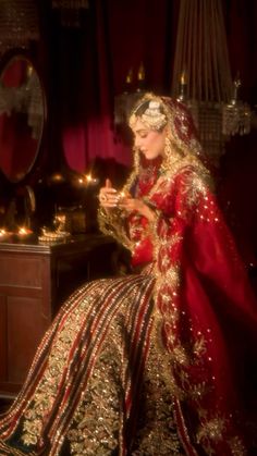 a woman in a red and gold wedding dress sitting on a chair looking at her cell phone