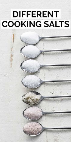 spoons filled with different types of cooking salts on top of each other in front of a white wall