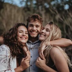 three people hugging each other and smiling at the camera with trees in the back ground