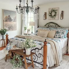 a bed sitting in a bedroom under a chandelier next to a table with flowers on it