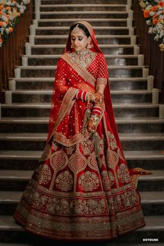 a woman in a red and gold bridal gown standing on stairs with flowers behind her