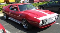 a red and white car parked in a parking lot next to other cars on the street