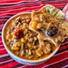 a hand holding a tortilla chip over a bowl of chili cheese and black bean soup