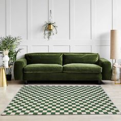 a green couch sitting on top of a checkered rug next to a lamp and potted plant