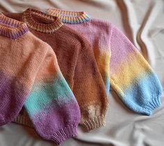 two knitted sweaters laying on top of a white bed next to each other