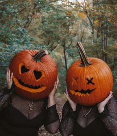 two women in black dresses holding pumpkins with faces carved into them