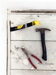 hammer, pliers and other tools laid out on a white wood planked surface