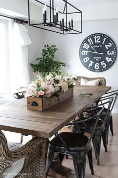 a dining room table with chairs and a large clock on the wall above it's head