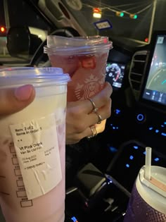 two people holding drinks in their hands while sitting in a car with the steering wheel behind them