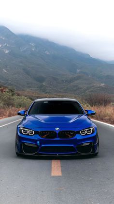 a blue car is driving down the road in front of some hills and trees with mountains behind it